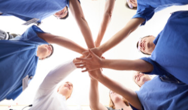 Team-Gefühl: Mitarbeiter stehen im Kreis, strecken ihren Arm nach vorne aus und legen ihre Hände übereinander